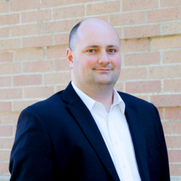 Headshot of Andrew Shaner. He wears a dark jacket with a white dress shirt under.