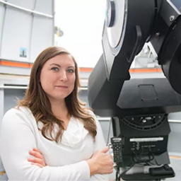 Bio headshot of Lindsay Fuller. Her arms are crossed and she stands in front of a large telescope.